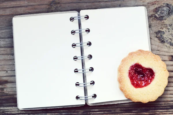 Zelfgemaakte koekjes met hartvormige jam en lege retro spiraal receptenboek over houten tafel — Stockfoto