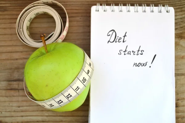 Diet concept with green apple, a notebook and a measuring tape on wooden table — Stock Photo, Image