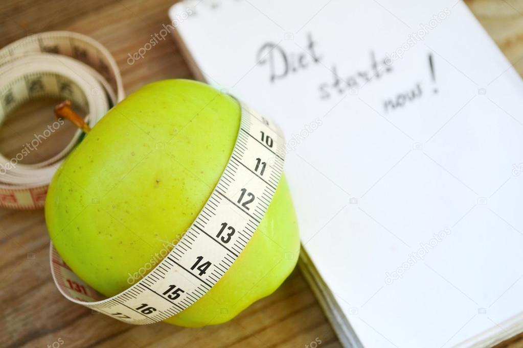 Diet concept with green apple, a notebook and a measuring tape on wooden table