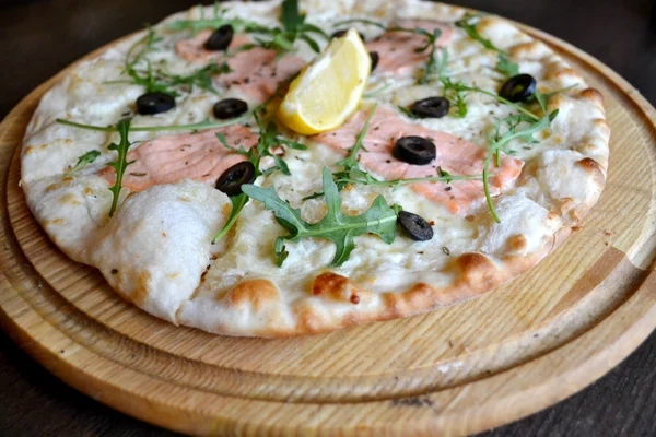 Pizza entière au saumon, citron et roquette sur assiette en bois — Photo