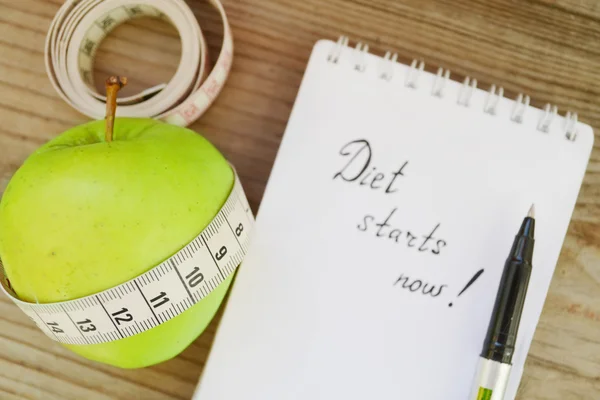 Diet concept with green apple, a notebook and a measuring tape on wooden table — Stock Photo, Image