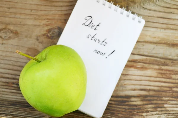 Diet concept with green apple, a notebook and a measuring tape on wooden table — Stock Photo, Image