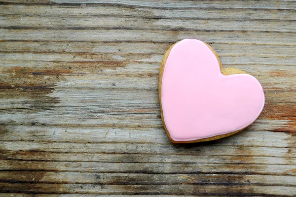 Gingerbread in a shape of heart with pink icing on wooden table — Stock Photo, Image