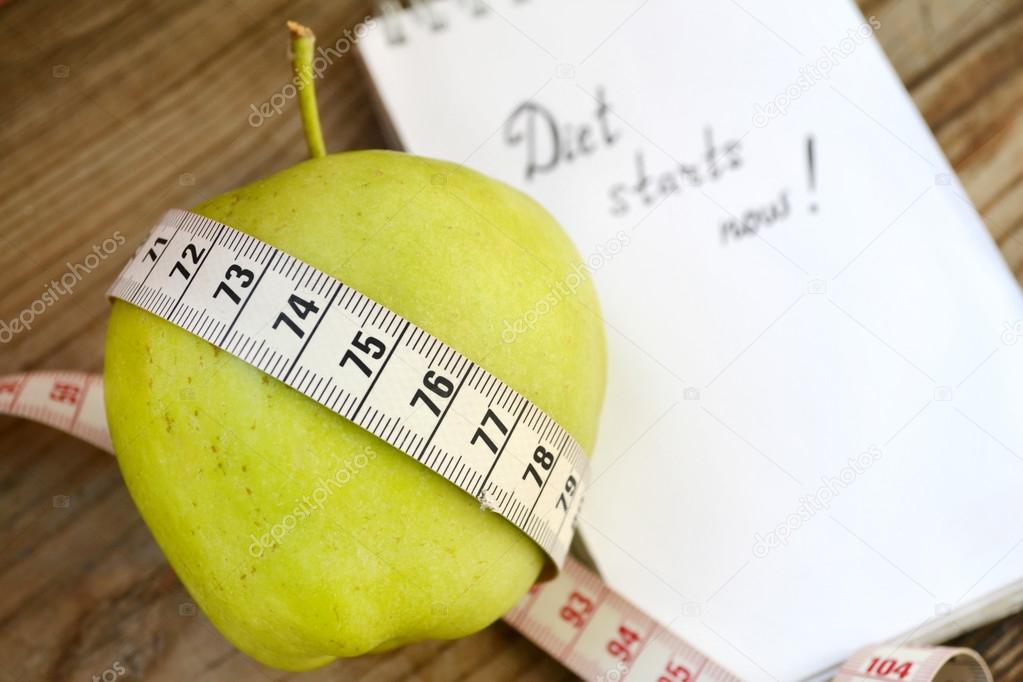 Diet concept with green apple, a notebook and a measuring tape on wooden table