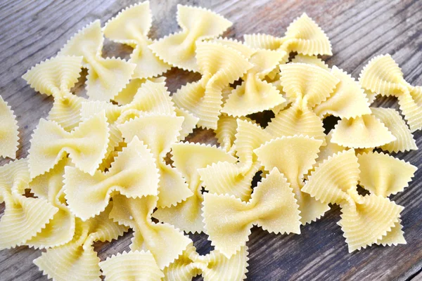 Borboleta não cozida em forma de macarrão farfalle na mesa de madeira — Fotografia de Stock