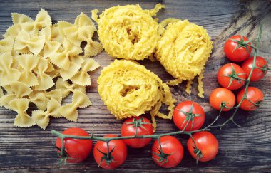 Küçük kırmızı kiraz domates ham makarna Reginette (Mafaldine) ile bir sürü ve şekilli makarna farfalle ahşap masa üzerinde Kelebek