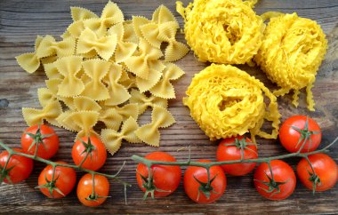 Küçük kırmızı kiraz domates ham makarna Reginette (Mafaldine) ile bir sürü ve şekilli makarna farfalle ahşap masa üzerinde Kelebek