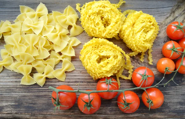 Bouquet de petites tomates cerises rouges aux pâtes crues Reginette (Mafaldine) et farfalle aux pâtes en forme de papillon sur table en bois — Photo