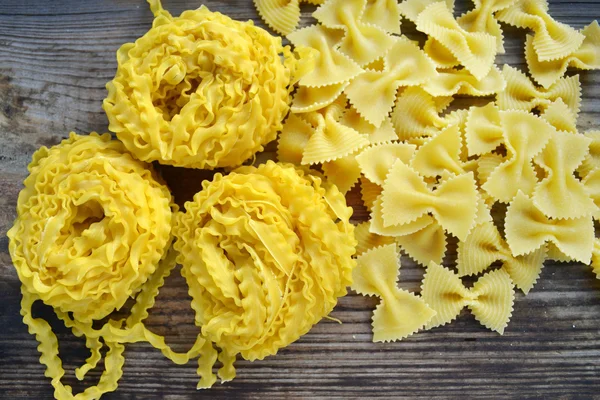 Massa små röda körsbärstomater med rå pasta Reginette (Mafaldine) och fjäril formad pasta farfalle på träbord — Stockfoto