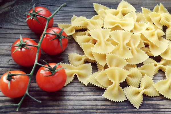 Mazzo di pomodorini rossi e farfalle di pasta a forma di farfalle sul tavolo di legno — Foto Stock