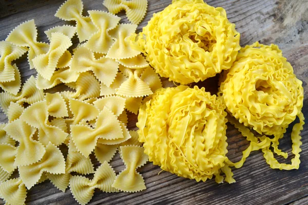 Rohe Pasta Reginette (Madaldine) und schmetterlingsförmige Pasta Farfalle auf Holztisch — Stockfoto