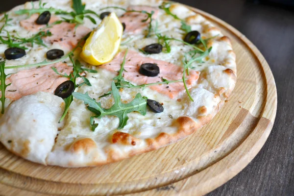 Pizza entière au saumon, citron et roquette sur assiette en bois — Photo