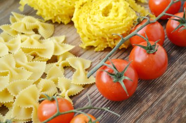 Küçük kırmızı kiraz domates ham makarna Reginette (Mafaldine) ile bir sürü ve şekilli makarna farfalle ahşap masa üzerinde Kelebek