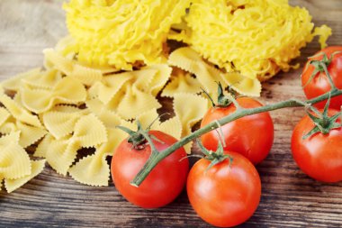 Küçük kırmızı kiraz domates ham makarna Reginette (Mafaldine) ile bir sürü ve şekilli makarna farfalle ahşap masa üzerinde Kelebek