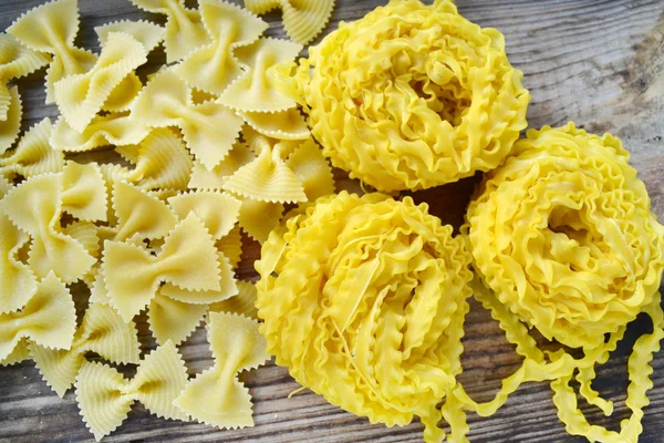 Rå pasta Reginette (Mafaldine) och fjäril formad pasta farfalle på träbord — Stockfoto