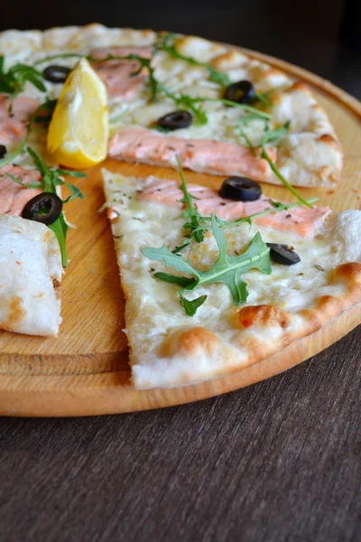 Cała pizza z łososia, cytryny i rukolą drewniana płyta — Zdjęcie stockowe