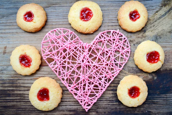 Concepto romántico con corazón rosa hecho a mano y un montón de galletas caseras con mermelada en la mesa de madera — Foto de Stock