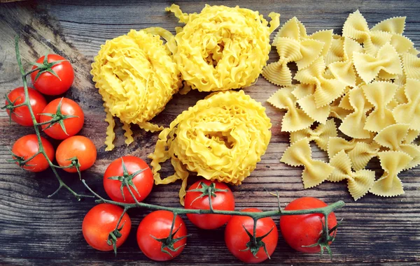 Mazzo di pomodorini rossi con pasta cruda Reginette (Mafaldine) e farfalle di pasta a forma di farfalla sul tavolo di legno — Foto Stock