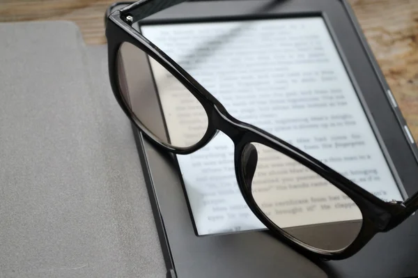 Černá ereader s retro brýle na dřevěný stůl — Stock fotografie