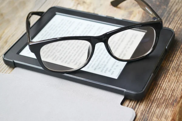 Black ereader with retro glasses on wooden table — Stock Photo, Image