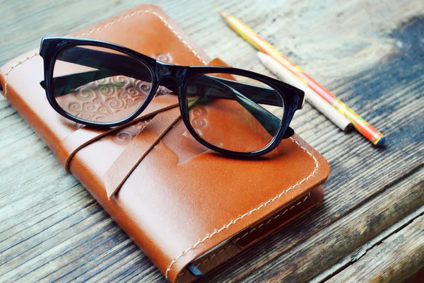 Ein altes Notizbuch in Ledereinband mit Bleistiften und Gläsern auf Holztisch — Stockfoto