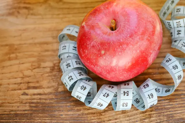 Concepto de dieta con manzana roja y cinta métrica azul en mesa de madera —  Fotos de Stock