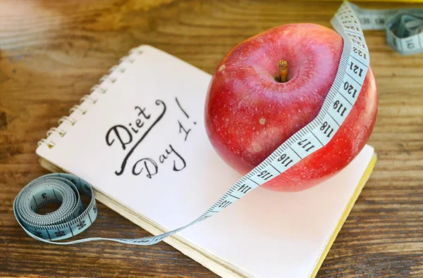 Diet concept with red apple, a notebook and blue measuring tape on wooden table — Stock Photo, Image