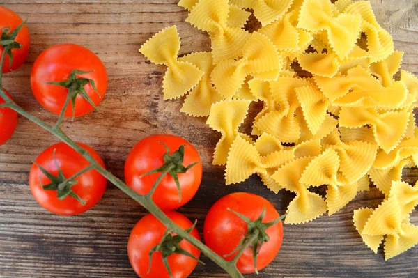 Mazzo di pomodorini rossi con pasta cruda Reginette (Mafaldine) e farfalle di pasta a forma di farfalla sul tavolo di legno — Foto Stock