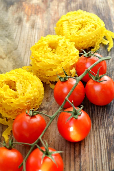 Mazzo di pomodorini rossi con pasta cruda Reginette (Mafaldine) sul tavolo di legno — Foto Stock