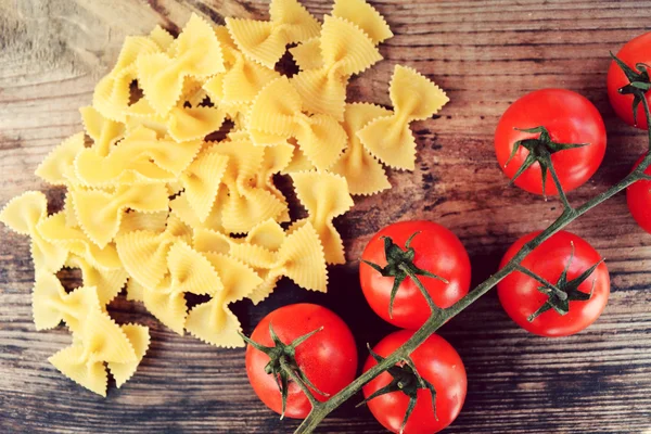 Mazzo di pomodorini rossi e farfalle di pasta a forma di farfalle sul tavolo di legno — Foto Stock