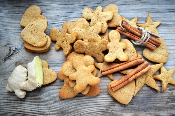 Gingerbread cookies in shapes of heart, star and man with cinnamon stick and ginger root on wooden table — Stock Photo, Image