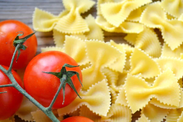 Mazzo di pomodorini rossi e farfalle di pasta a forma di farfalle sul tavolo di legno — Foto Stock