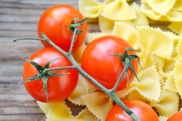 Mazzo di pomodorini rossi e farfalle di pasta a forma di farfalle sul tavolo di legno — Foto Stock