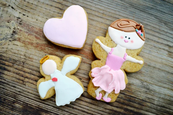 Gingerbread in a shape of heart and angel with pink and white icing and little cute ballet dancer on wooden table — Stock Photo, Image