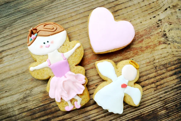 Gingerbread in a shape of heart and angel with pink and white icing and little cute ballet dancer on wooden table — Stock Photo, Image