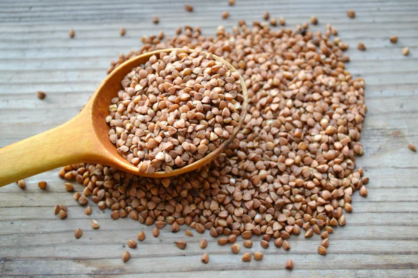 Buckwheat grains with an old big spoon on wooden table — Stock Photo, Image