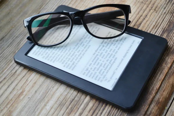 Black ereader with retro glasses on wooden table — Stock Photo, Image