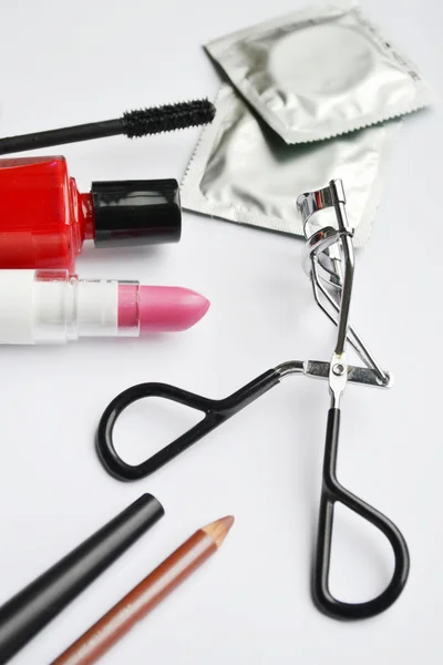 Paar van condooms en een cosmetica bezet met zwarte mascara, roze en rood nagellak en lippenstift en wimper krultang geïsoleerd op wit — Stockfoto