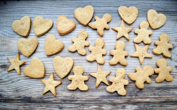 Gingerbread cookies in shapes of heart, star and man with cinnamon stick and ginger root on wooden table
