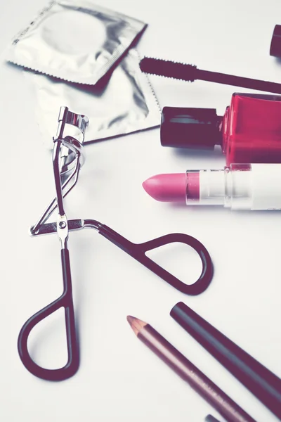 Ein paar Kondome und ein Kosmetik-Set mit schwarzer Mascara, rosa und rotem Nagellack sowie Lippenstift und Wimpernzange isoliert auf weiß — Stockfoto