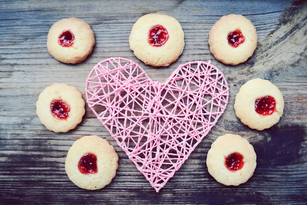 Romantic concept with handmade pink heart and lots of homemade cookies with jam on wooden table — Stock Photo, Image