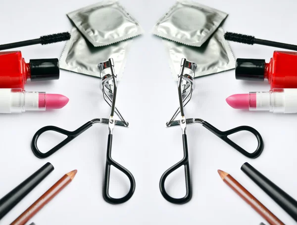 Couple of condoms and a cosmetics set with black mascara, pink and red nail polish and lipstick and eyelash curler isolated on white — Stock Photo, Image