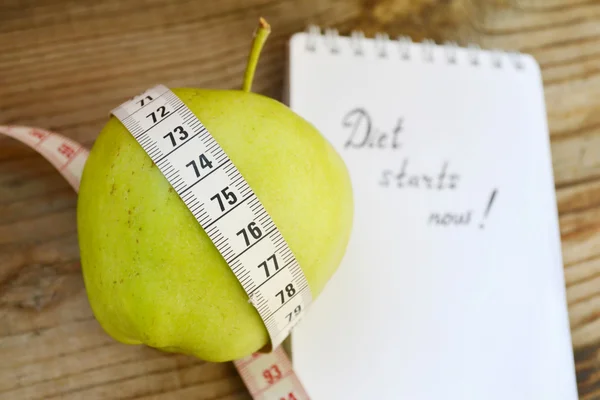 Diet concept with green apple, a notebook and a measuring tape on wooden table — Stock Photo, Image