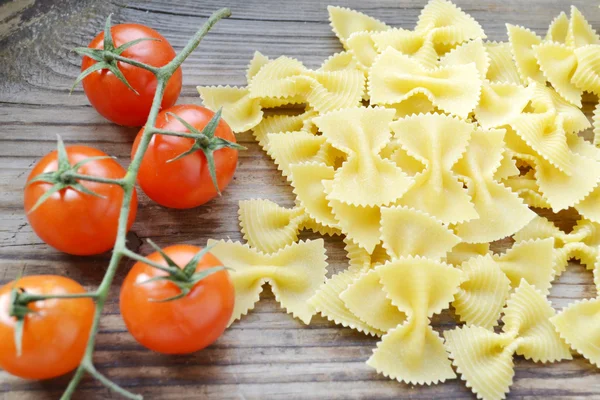 Csomó kis piros cherry paradicsom és a pillangó alakú tészta farfalle fa tábla — Stock Fotó