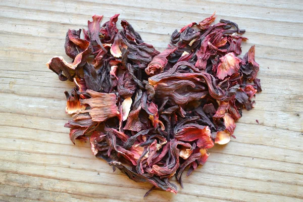 Folhas secas e pétalas de chá de hibisco em forma de coração na mesa de madeira — Fotografia de Stock