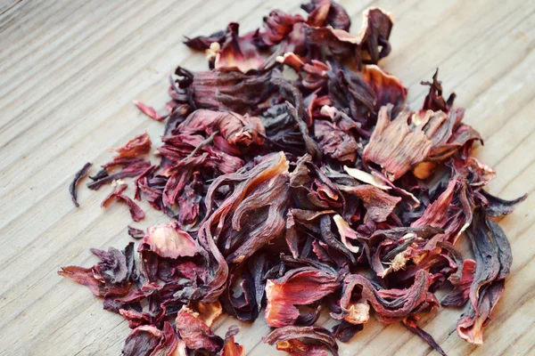 Dry leaves and petals of hibiscus tea on wooden table — Stock Photo, Image