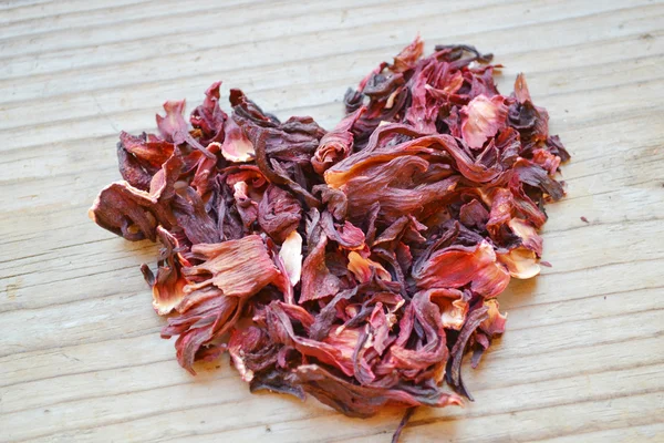 Foglie secche e petali di tè di ibisco in una forma di cuore su tavolo di legno — Foto Stock