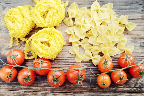 Mazzo di pomodorini rossi con pasta cruda Reginette (Mafaldine) e farfalle di pasta a forma di farfalla sul tavolo di legno — Foto Stock