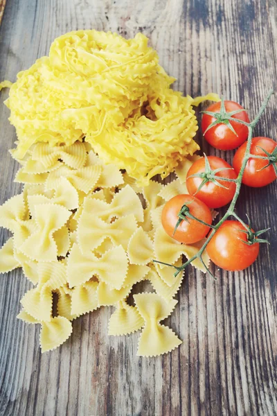 Massa små röda körsbärstomater med rå pasta Reginette (Mafaldine) och fjäril formad pasta farfalle på träbord — Stockfoto