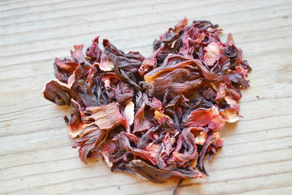 Dry leaves and petals of hibiscus tea in a shape of heart on wooden table — Stock Photo, Image